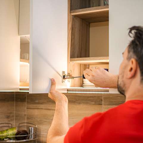 Monteur justiert das Scharnier eines Hängeschranks.