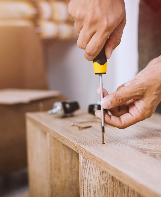 Hand verschraubt ein Möbelbauteil aus Holz mit Schraubendreher.