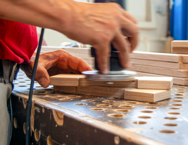 Holzbauteil wird an einer Werkbank maschinell geschliffen.