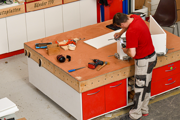 Mitarbeiter montiert ein Möbelbauteil an einer Werkbank.