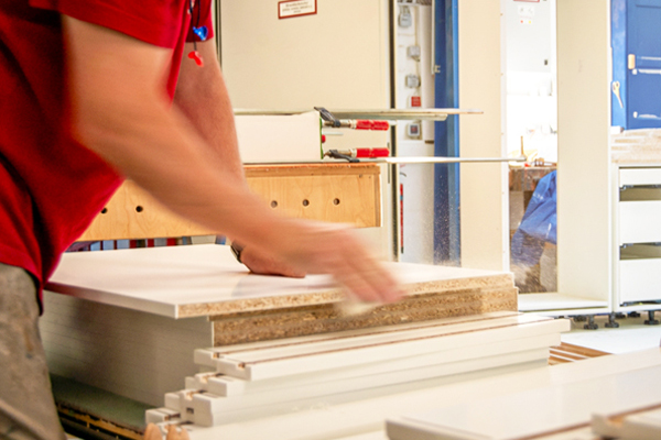 Mitarbeiter stapelt und bearbeitet Möbelbauteile in einer Werkstatt.